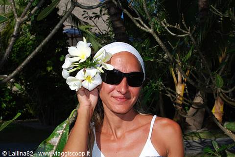 Woman in white bandana and sunglasses holding plumeria flowers among palms