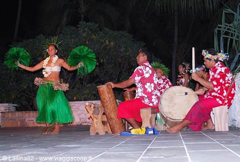 Dancer in green skirt with flowers performs beside drummers in red aloha shirts