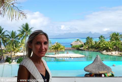 Blonde smiling woman in front of tropical pool with palms and thatched hut