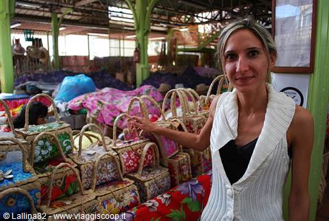 Blonde woman touches colorful woven bags at Maputo's covered market