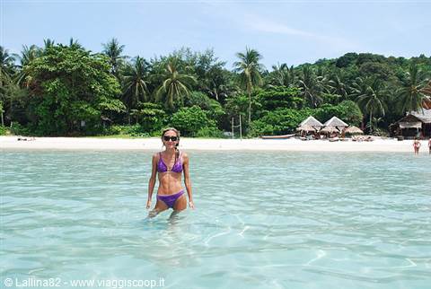 Woman in purple bikini wading in turquoise water by palm-fringed beach bungalows