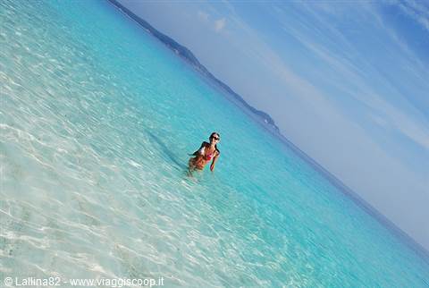 Woman in red swimsuit swimming in clear turquoise sea, mountains in distance