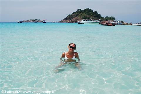 Girl sitting in turquoise water with boats and green island behind