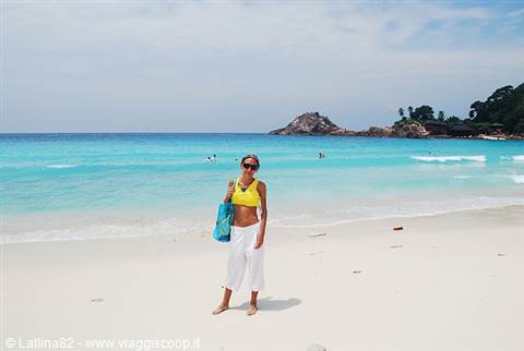 Woman in yellow top and white pants on sandy beach, turquoise sea