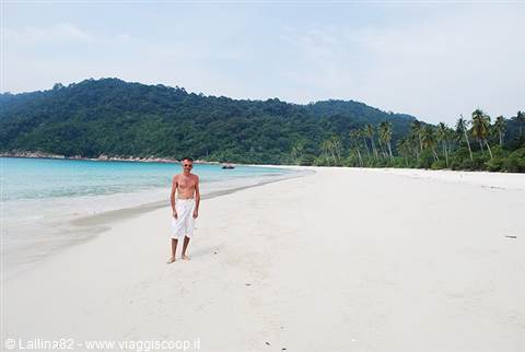 Man in white towel walks on white sand beach lined with palms