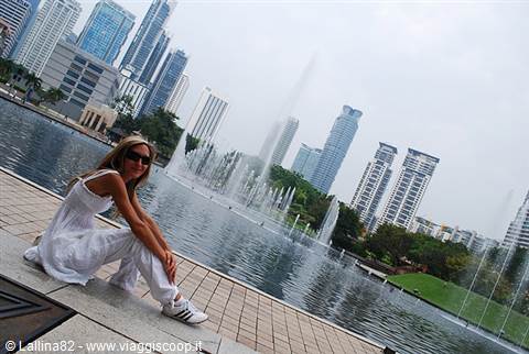 Girl in white sitting by the lake fountains with Kuala Lumpur skyscrapers behind