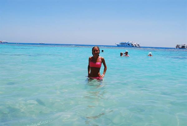 Woman in pink bikini in turquoise water with yachts in background