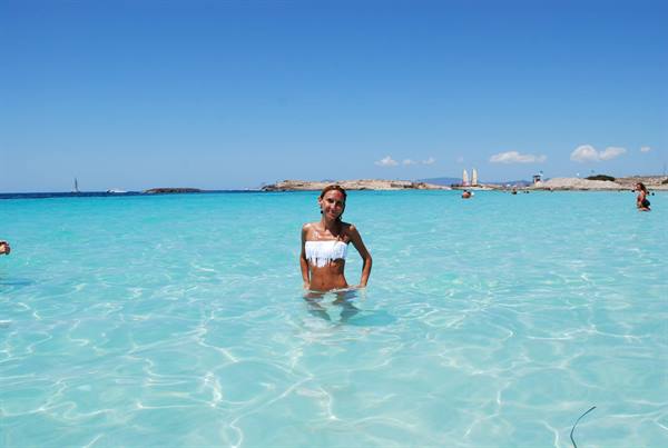 Woman in white bikini in turquoise water, sandy beach, blue sky, swimmers nearby