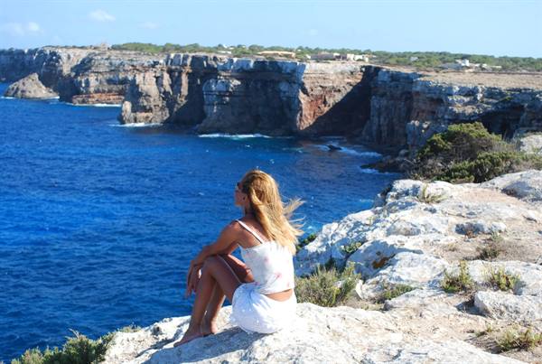 Blonde woman sitting on limestone rocks above blue sea cliffs