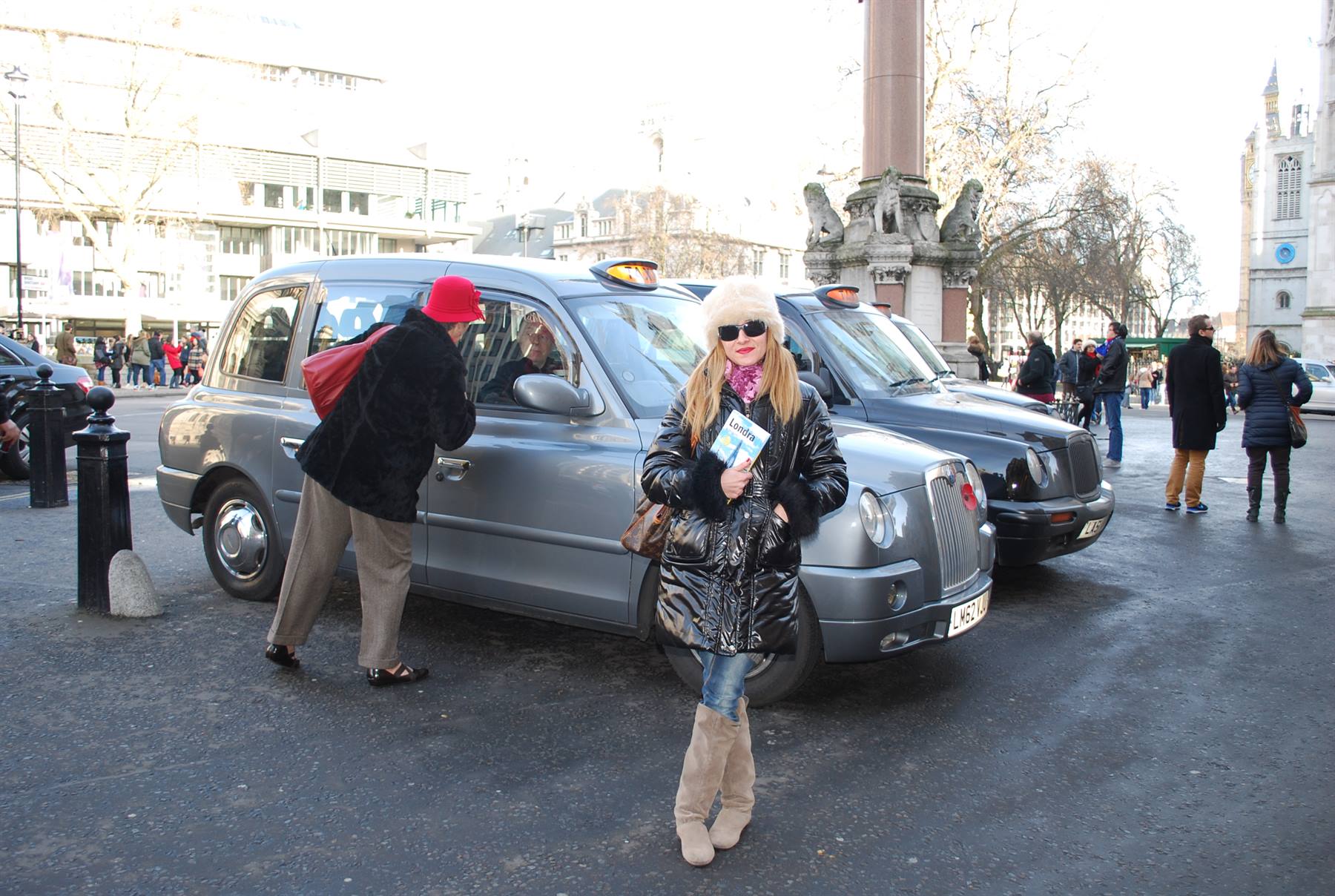 Donna con cappello bianco accanto ai taxi neri londinesi a Westminster