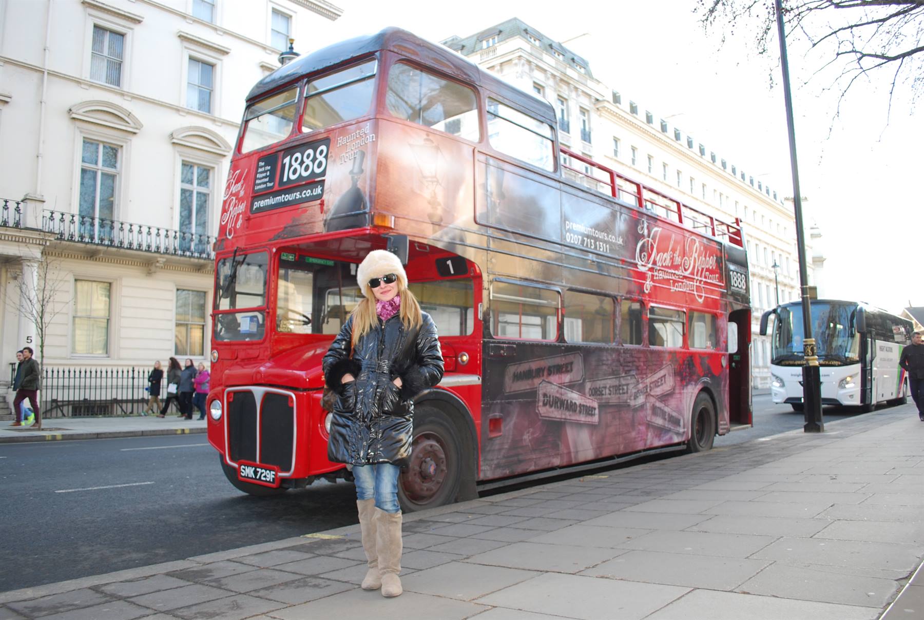 Donna con cappello bianco e piumino davanti a un autobus a due piani rosso a Londra