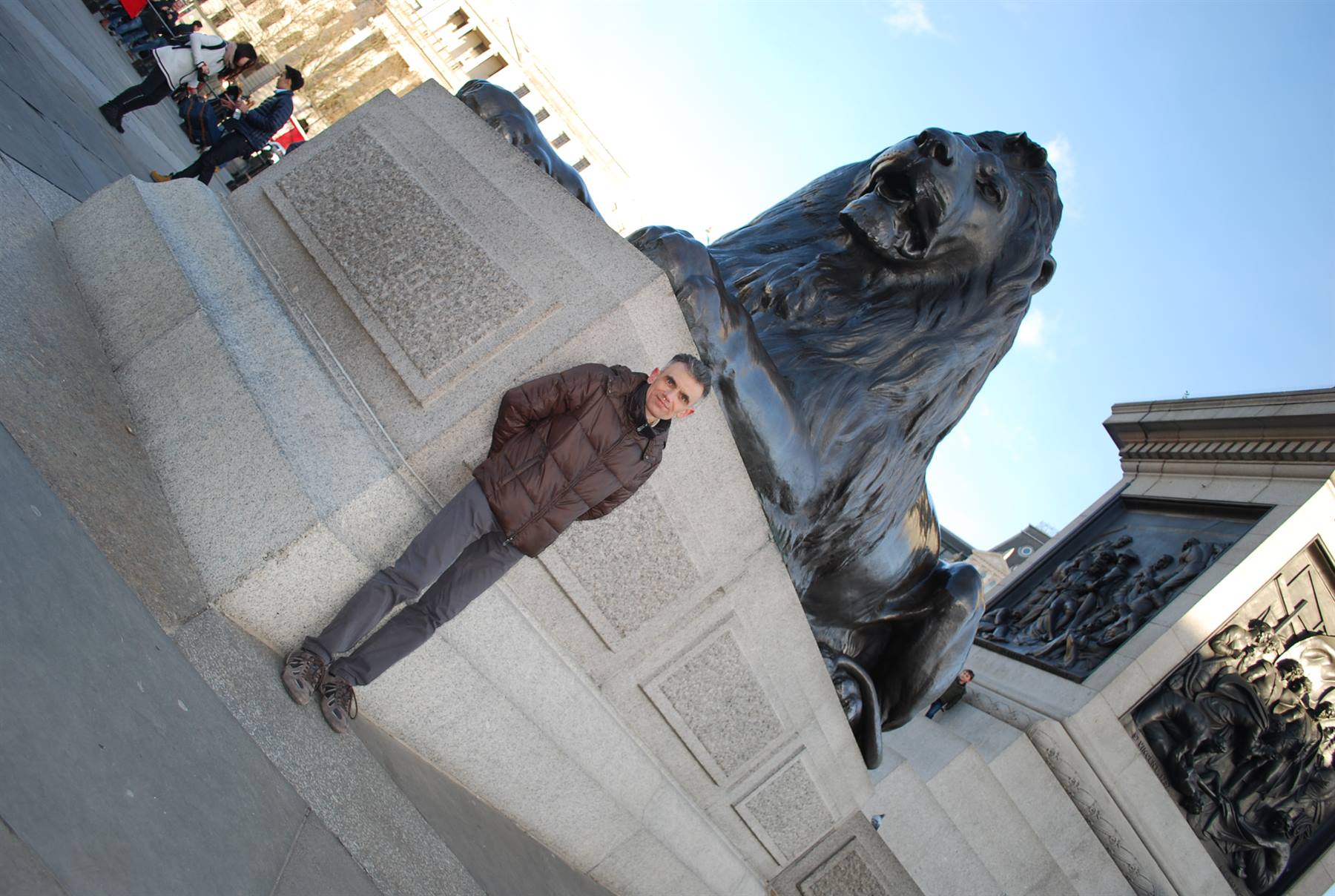 Uomo posa accanto al leone di bronzo della base di Nelson a Trafalgar Square