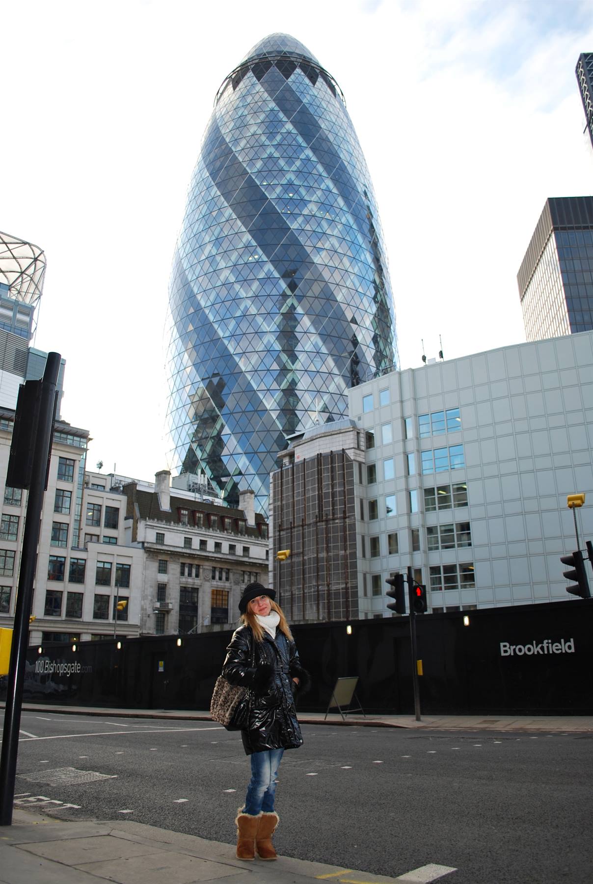 Donna in cappotto nero incrocia la strada davanti al grattacielo Gherkin a Londra
