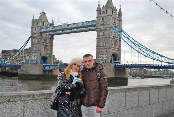 Smiling couple in winter clothes in front of London's Tower Bridge