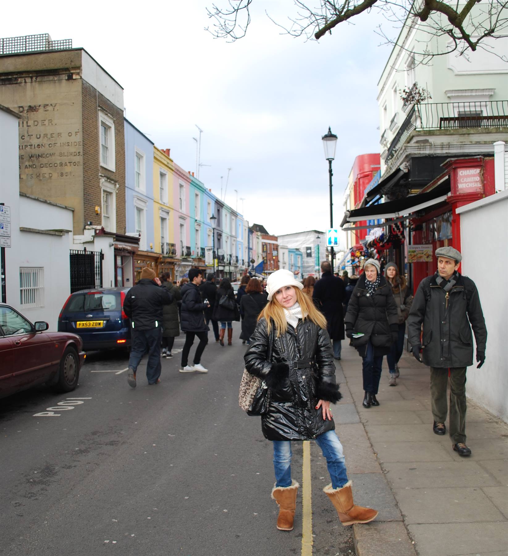 Ragazza in cappotto nero posa in strada tra le case colorate di Portobello Road