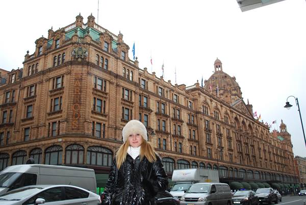 Woman in white hat in front of Harrods department store in London, traffic around