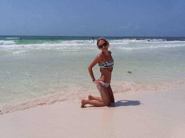 Woman in bikini kneeling on white sand, turquoise waves behind