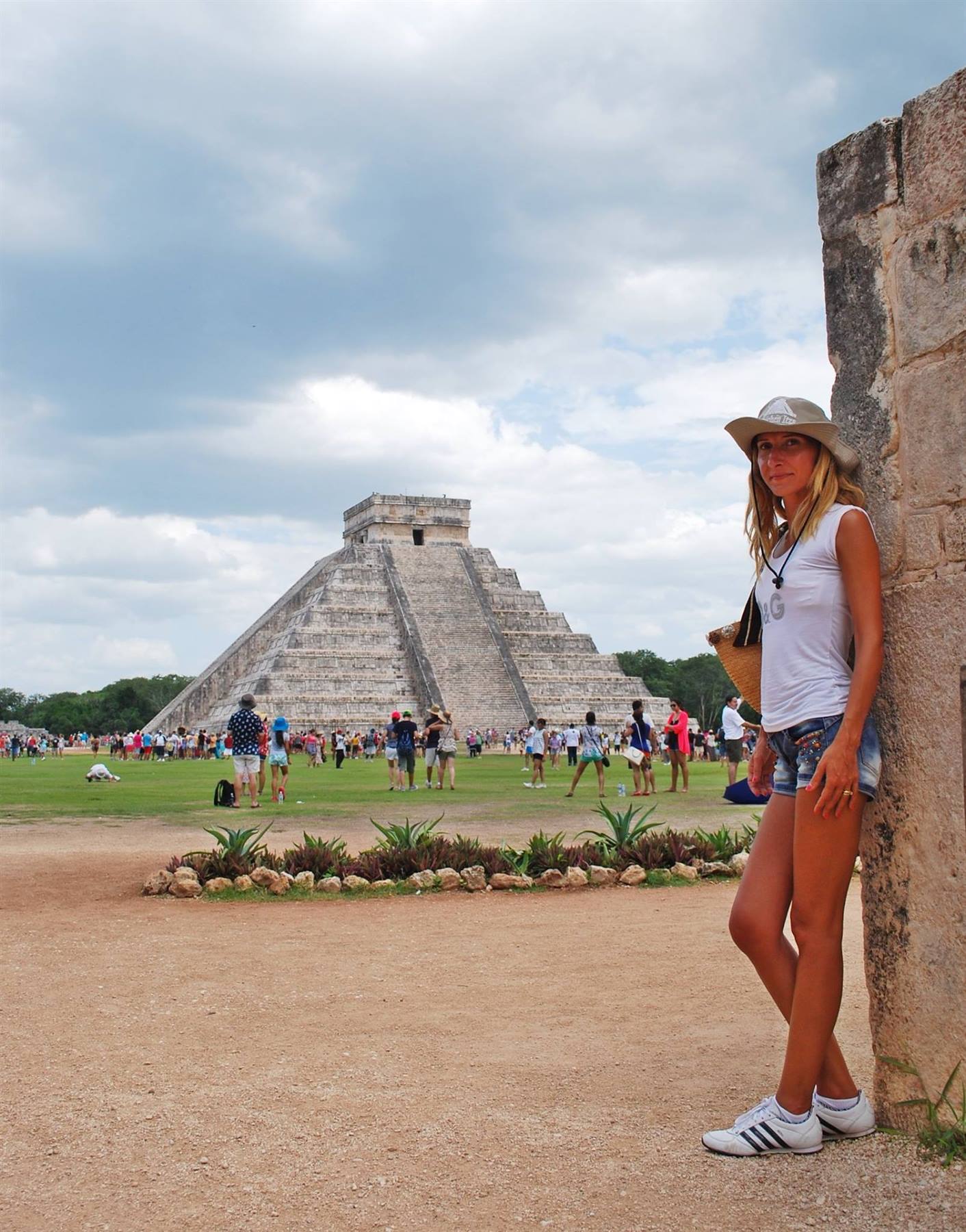 Turista col cappello appoggiata a un muro di pietra davanti a Chichén Itzá