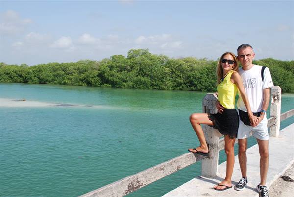 Couple posing on concrete bridge in front of turquoise lagoon with green mangroves