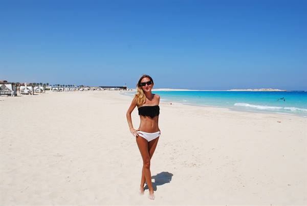 Woman in black and white bikini on white sand, turquoise ocean, sunny beach with umbrellas