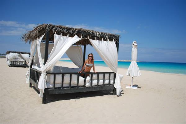 Woman in bikini inside a wooden gazebo with white curtains on sandy beach
