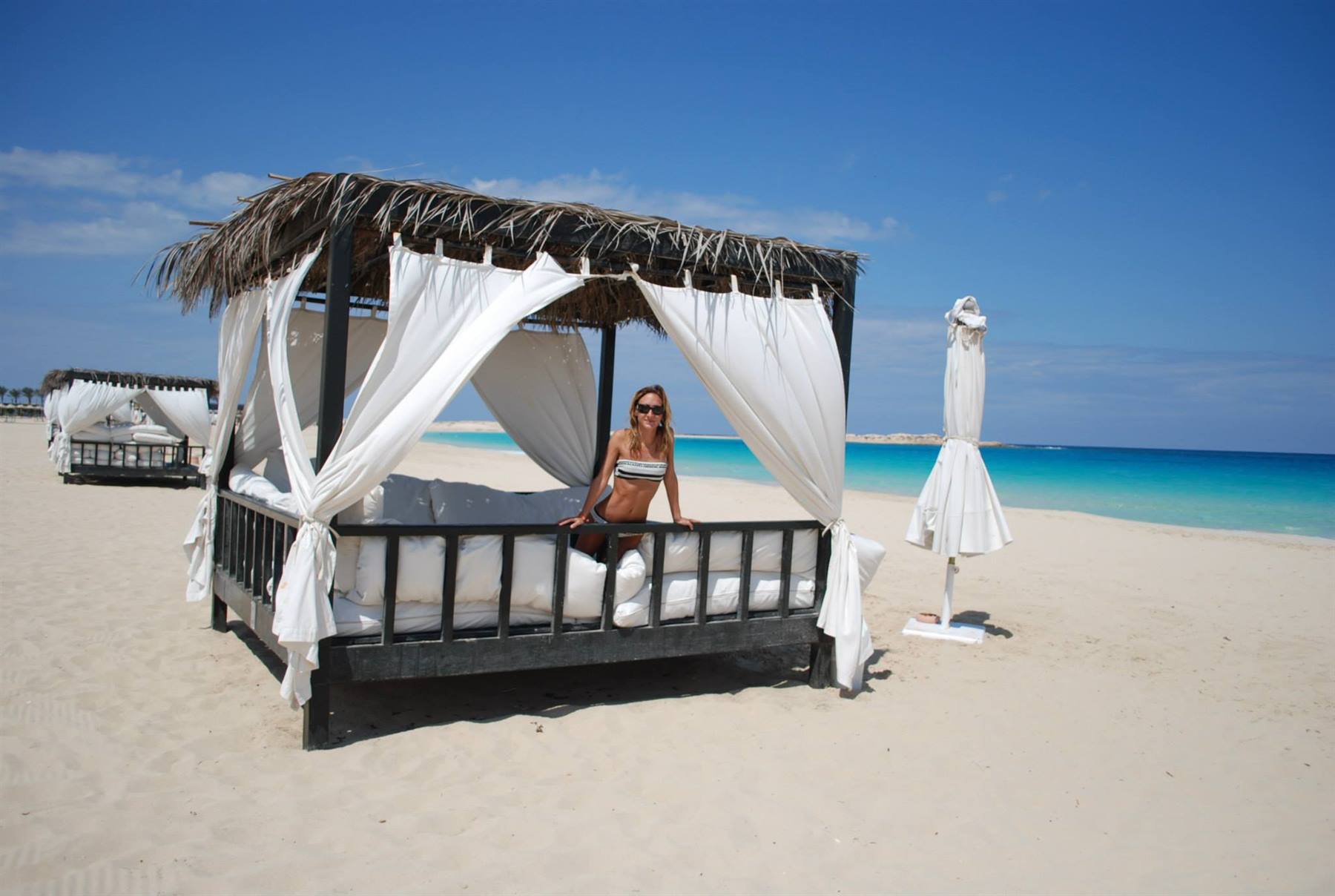 Donna in bikini dentro un gazebo di legno con tende bianche su spiaggia sabbiosa