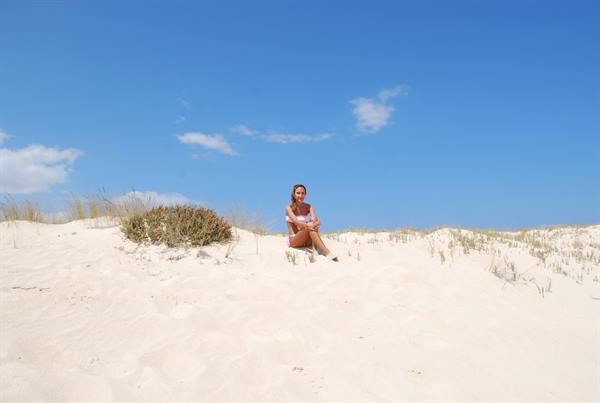 Woman sitting on white sand dune among sparse plants, blue sky