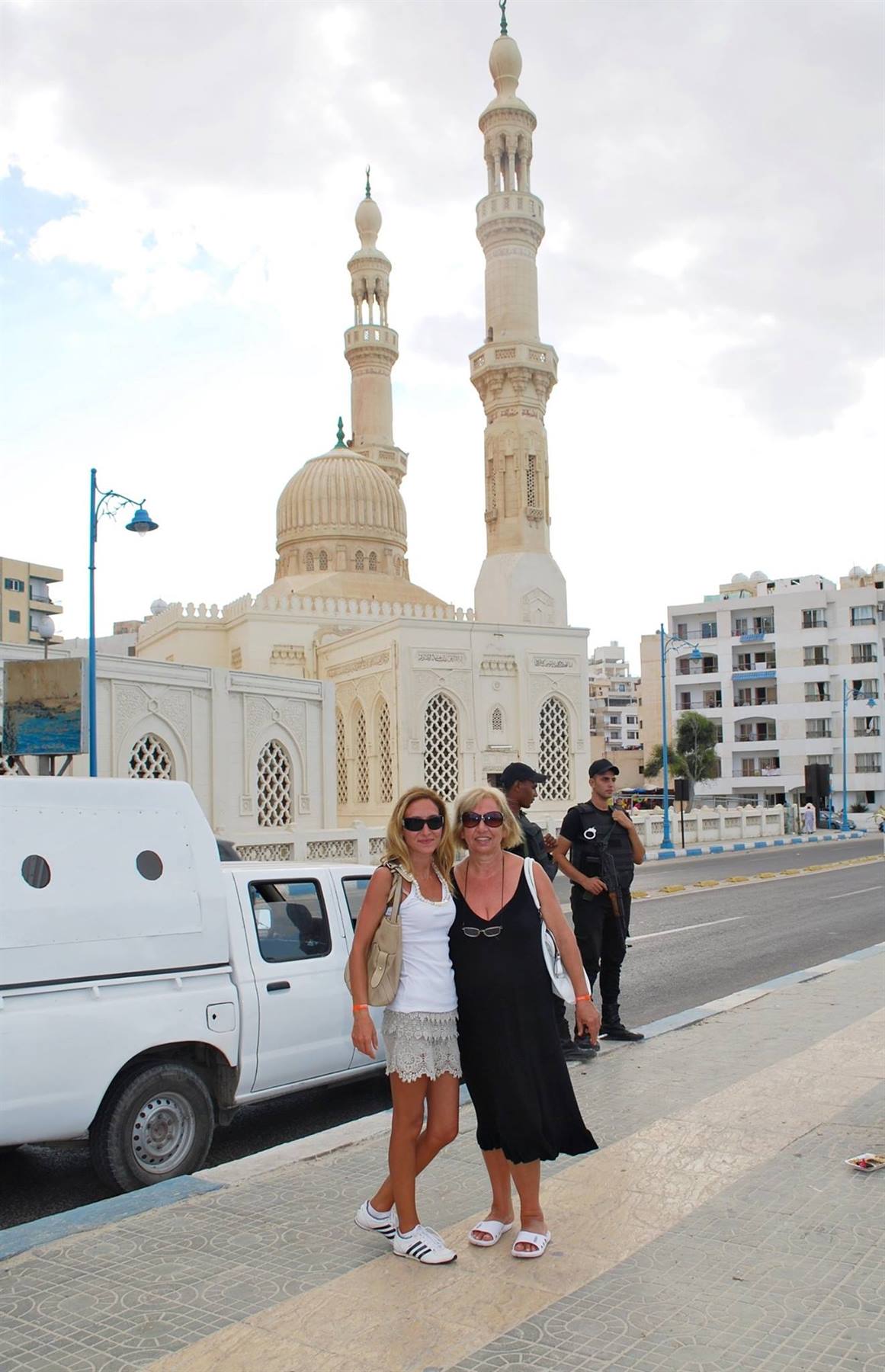 Due turiste posano sulla strada davanti a una moschea bianca con minareto