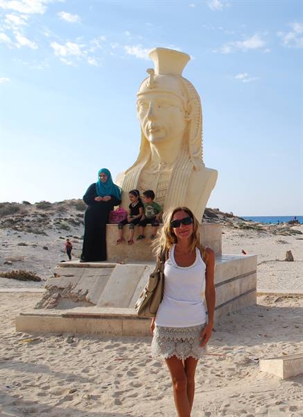 Woman in white before Cleopatra statue on the beach, family seated on base
