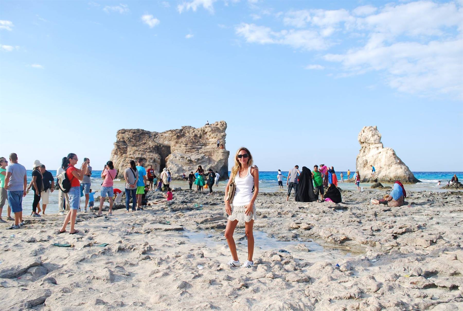 Turista in bianco posa sulla spiaggia rocciosa con formazioni calcaree e bagnanti