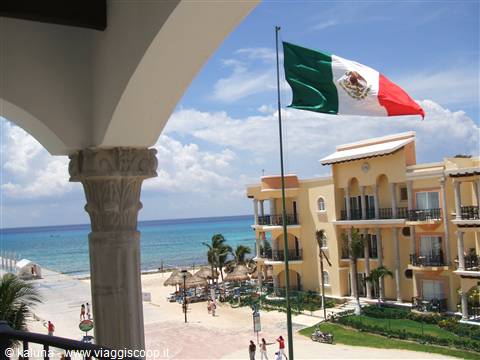 Mexican flag waves over yellow hotel by the Caribbean beach