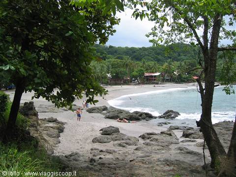 Sandy beach with rocks and tourists among lush tropical trees