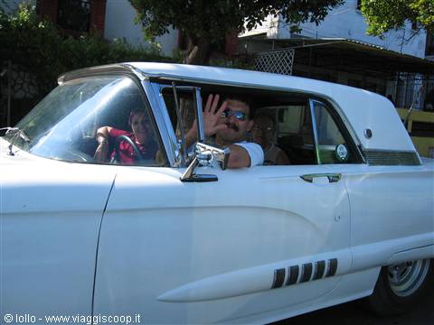 Tourists wave from a vintage white car under the sun