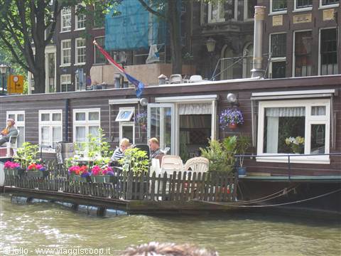 Wooden houseboat on Amsterdam canal, people relaxing on a flower-filled deck