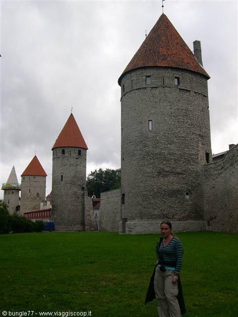 Medieval stone towers with red roofs in Tallinn, woman posing on the grass