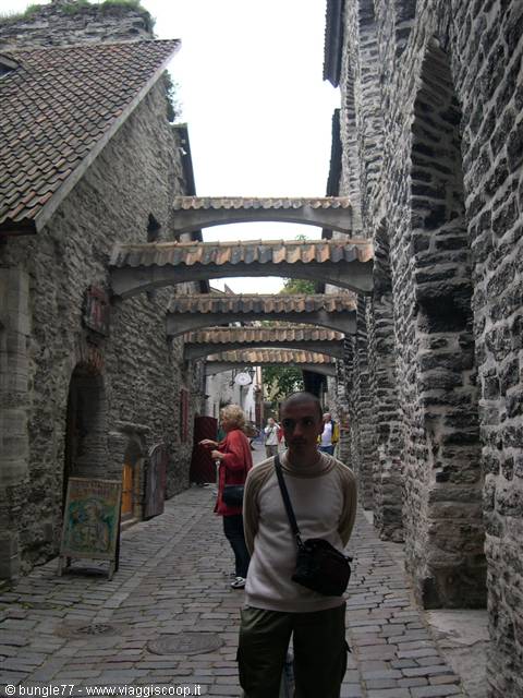 Man standing in St. Catherine's Passage, Tallinn, with stone walls and tiled arches