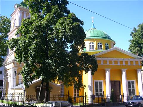 Yellow church with green dome and white colonnade, trees and cars in front