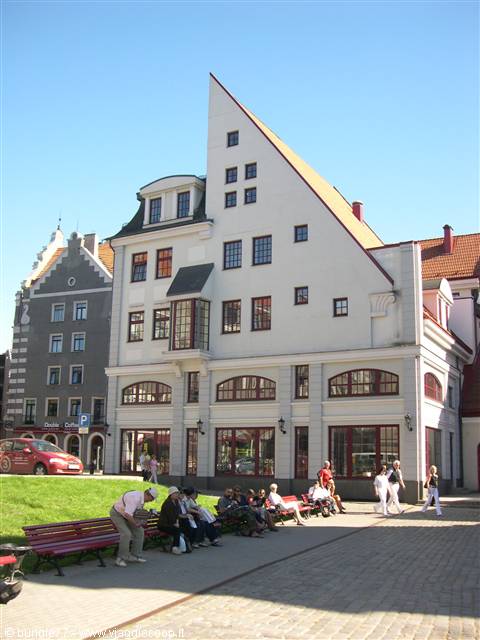 People sitting on benches in front of a white wedge-shaped building in Tallinn