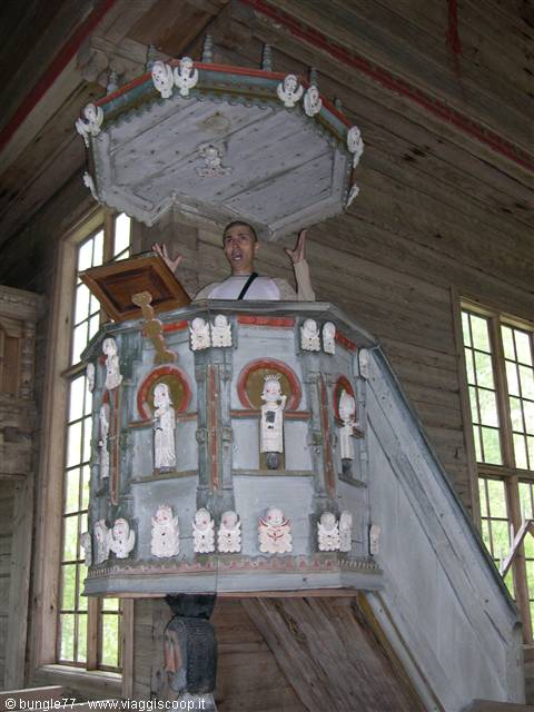 Man gestures from the carved wooden pulpit of a wooden church