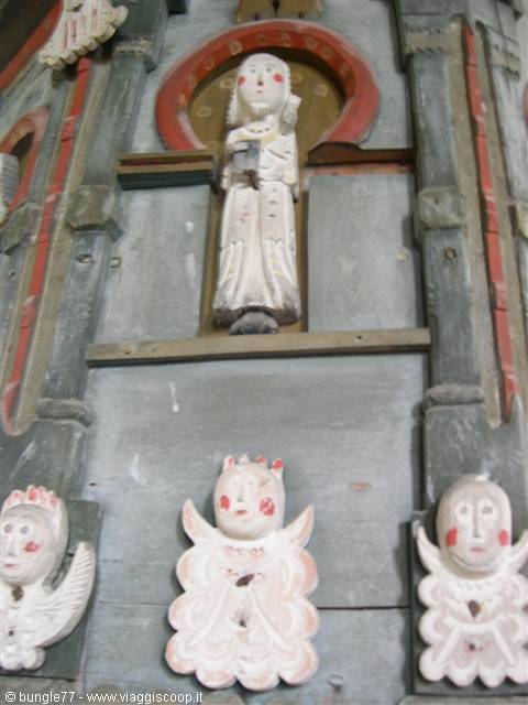 Painted wooden saint statue with carved angels on church facade