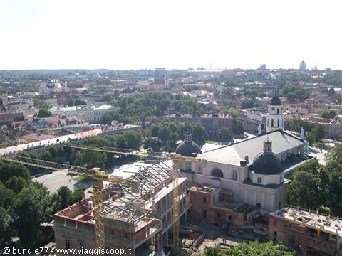 Construction site with cranes beside Vilnius Cathedral, rooftops and trees under bright sky