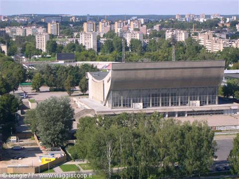 Curved-roof sports hall among trees, Soviet apartment blocks in the background