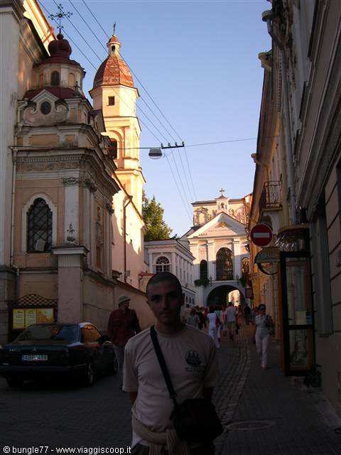 Man posing on cobbled street with baroque church and historic gate, Vilnius