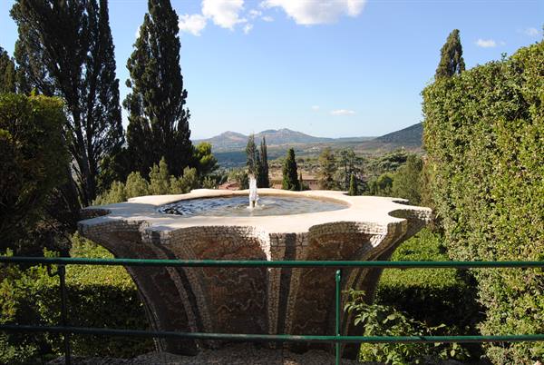 Flower-shaped mosaic fountain among cypresses, hills behind