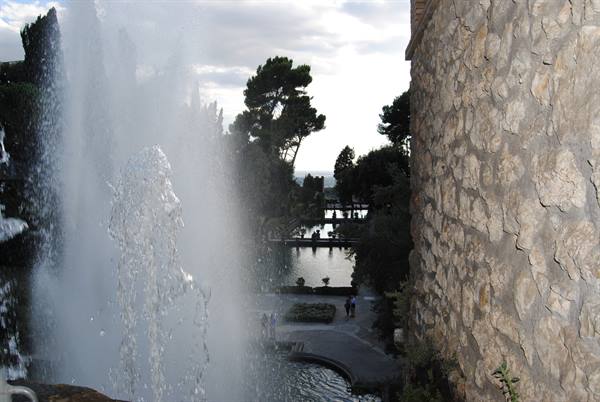Water fountain beside a rough stone wall, garden ponds and pines below