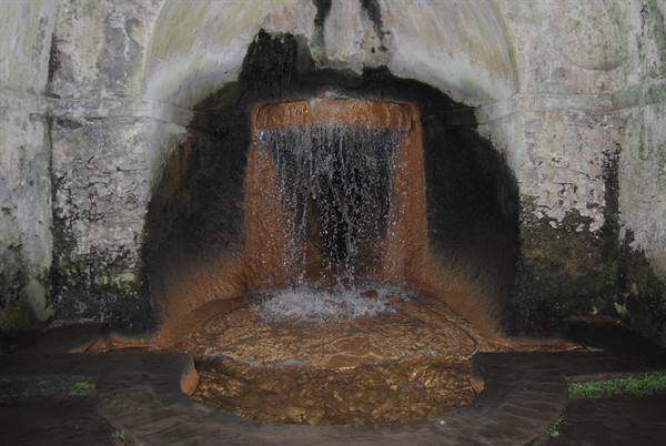 Iron-rich water flows from a mineral-crusted stone spout beneath a dark vault