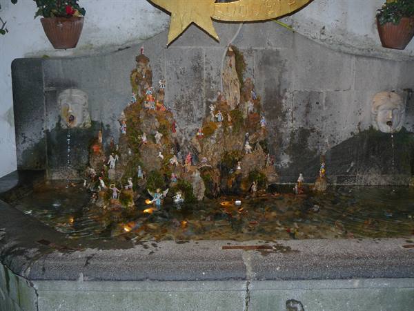 Stone fountain with mossy nativity figures, water-spouting masks and golden star