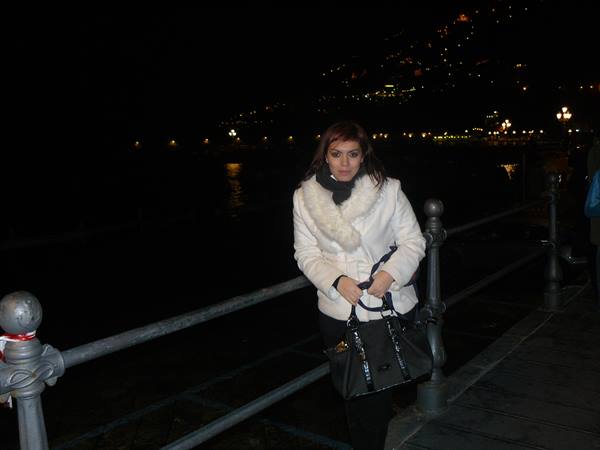 Woman with handbag leaning on metal railing, night lights along the waterfront