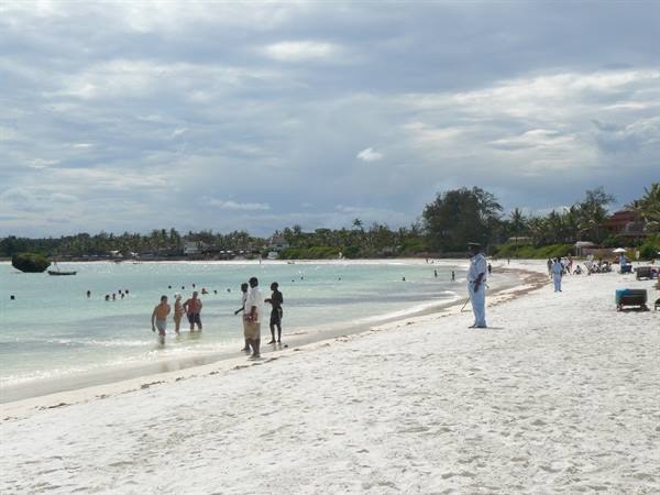 Tourists and vendors on white sand, turquoise water, cloudy sky