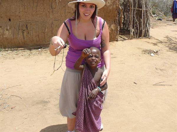 Tourist in hat beside a Maasai child in front of mud huts